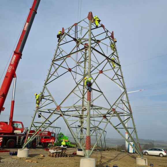 Des électriciens Cteam travaillent sur une tour pylône électrique, soulevant une structure métallique lourde avec une grue. Des électriciens Cteam travaillent sur une tour pylône électrique, soulevant une structure métallique lourde avec une grue.