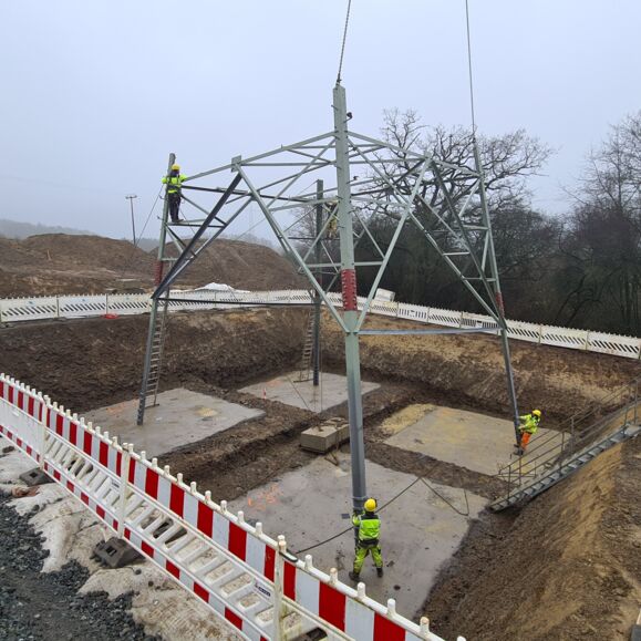 Construction d'un pyl&ocirc;ne de transport d'&eacute;lectricit&eacute; par Cteam, avec des ouvriers travaillant en hauteur et au sol sur le chantier.
